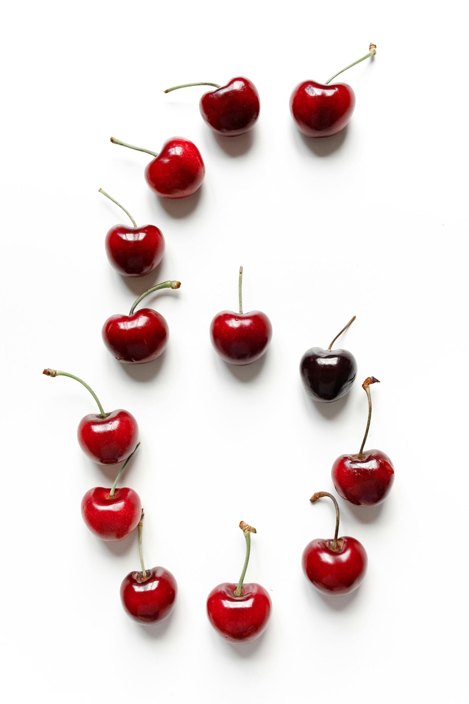 Vibrant red cherries artfully arranged in the shape of the number six on a white background.